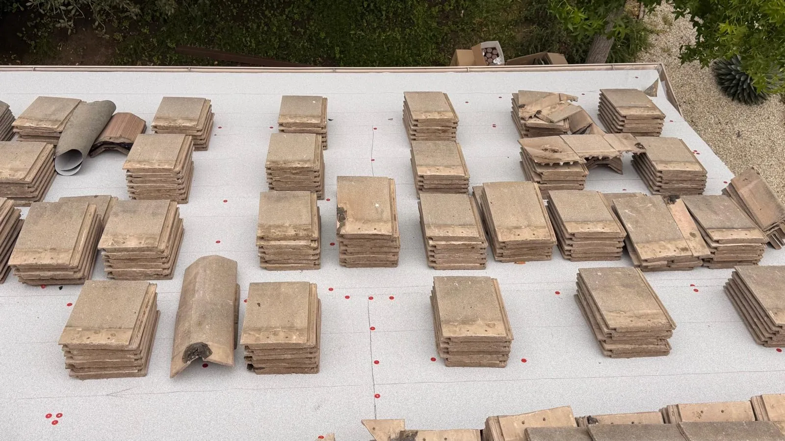Concrete roof tiles staged on new underlayment, with a few cracked tiles set aside